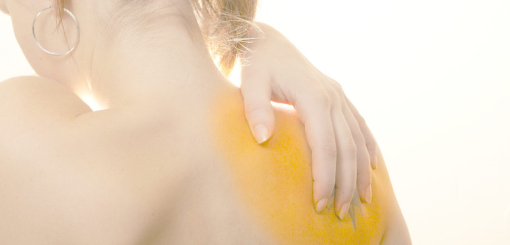 Photo showing the back of a woman with a sore shoulder. Her hand is on her shoulder.