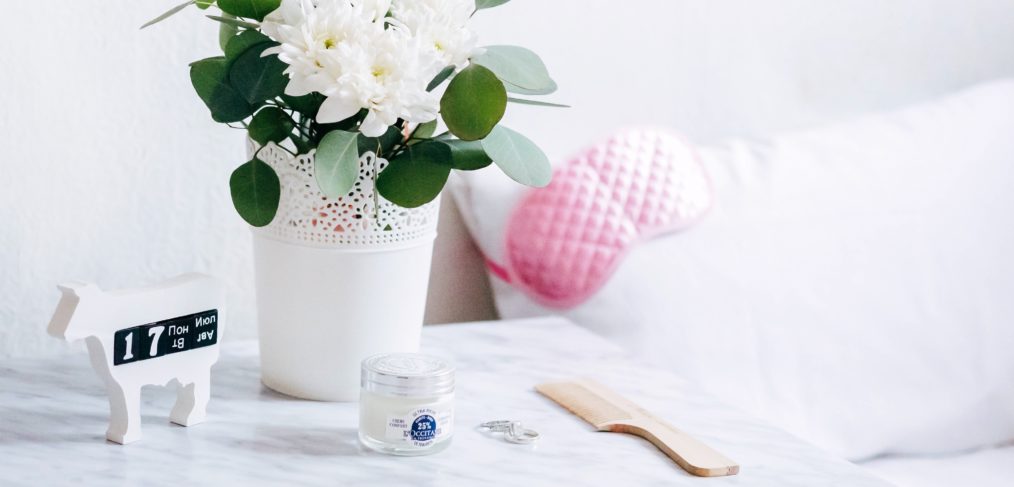 Bedside marble table with a white flower pot, a comb, two wedding rings and a clear cream jar.