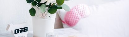 Bedside marble table with a white flower pot, a comb, two wedding rings and a clear cream jar.