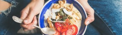 Yogurt, granola, seeds, fresh and dry fruits and honey in blue ceramic bowl in woman' s hands.