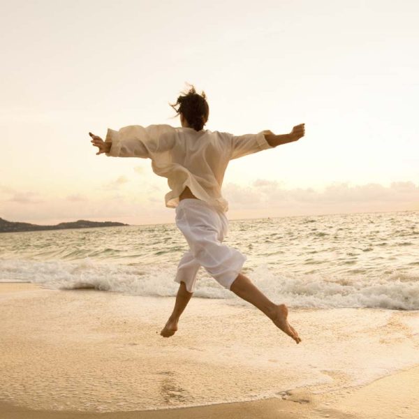 Woman embracing freedom, dancing along sandy beach with outstretched arms and waves at her feet