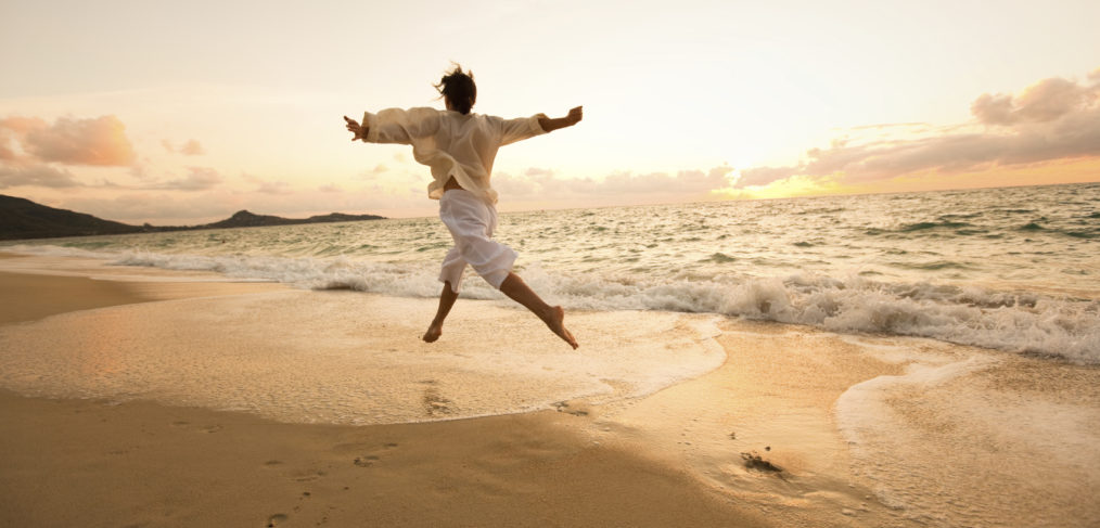 Woman embracing freedom, dancing along sandy beach with outstretched arms and waves at her feet