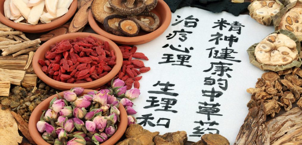 Chinese herbs used in alternative herbal medicine with calligraphy script on rice paper. Translation reads as traditional ancient chinese medicine to heal mind, body and spirit.