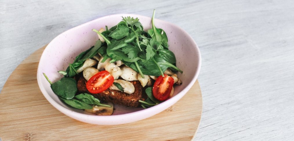 A picture of some tomatoes, spinach and bread in a pink bowl.