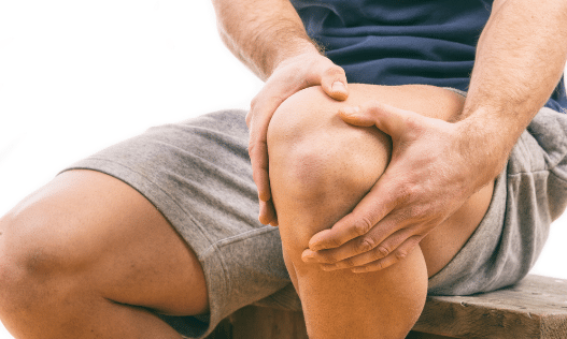 A man sitting down with both his hands on one of his knees.