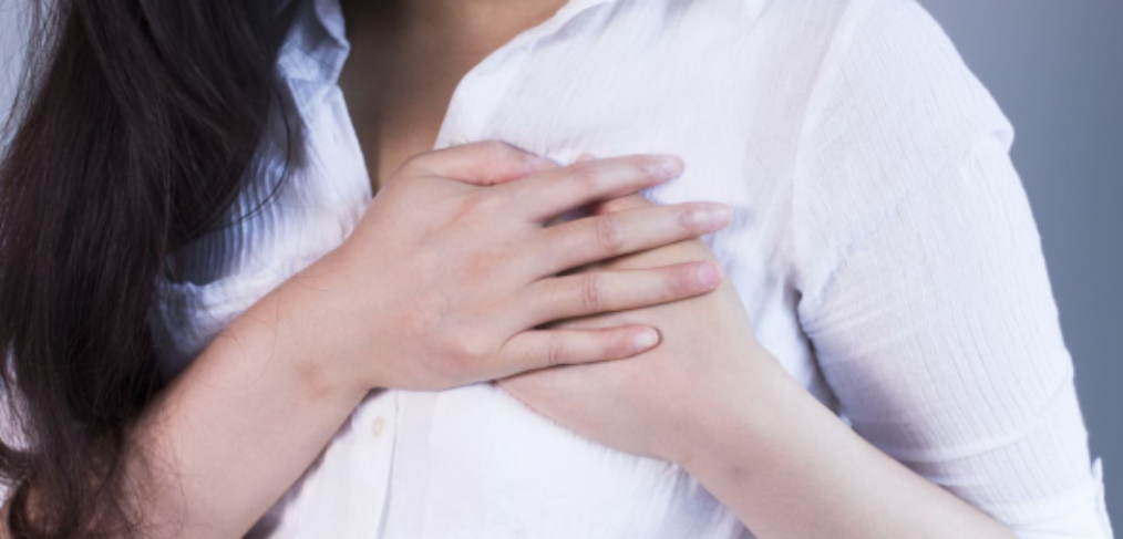 Woman in a white shirt holding both her hands close to her left breast