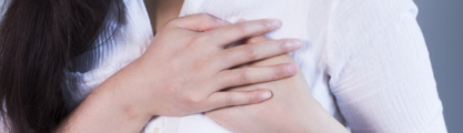 Woman in a white shirt holding both her hands close to her left breast