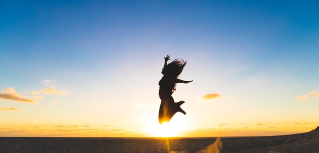 Woman jumping in the air with a sunset behind her