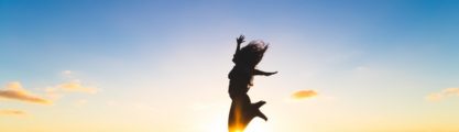 Woman jumping in the air with a sunset behind her