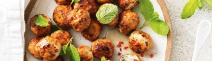 meatballs on a plate with fresh herbs and a bowl of chilli sauce with a spoon in it