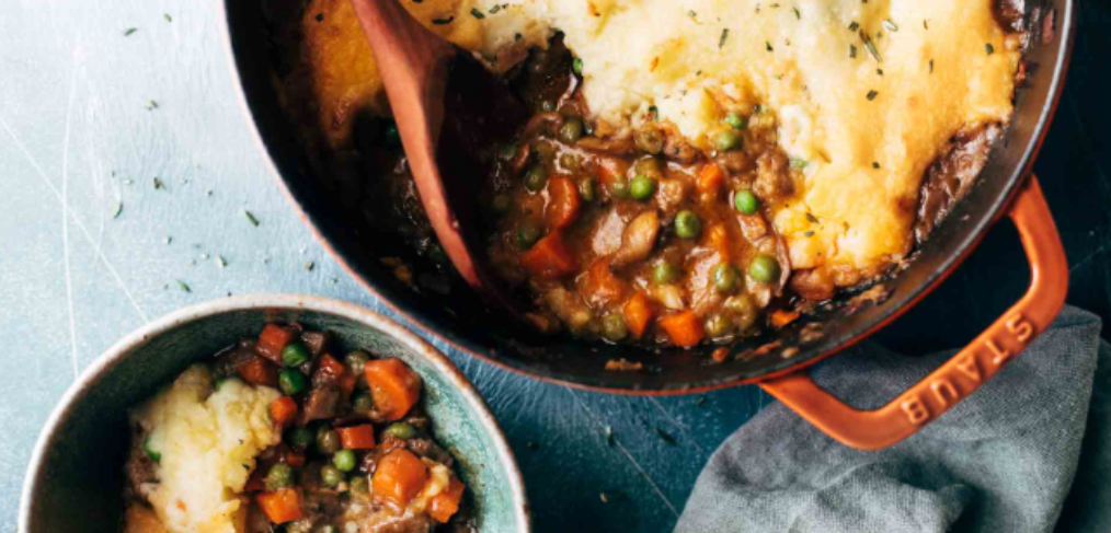 Shepherds pie consisting of mashed potato and a mixture of vegetables in a gravy underneath served in a casserole dish