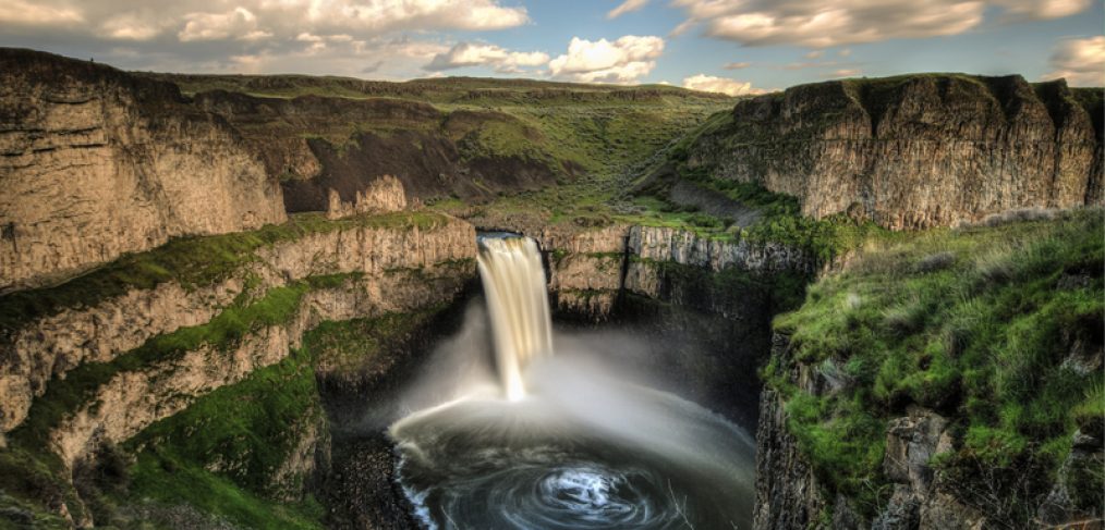 Landscape featuring rocky escarpments and green grass and a waterfall flowing into a pool