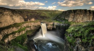 Landscape featuring rocky escarpments and green grass and a waterfall flowing into a pool