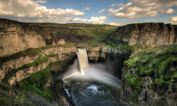 Landscape featuring rocky escarpments and green grass and a waterfall flowing into a pool